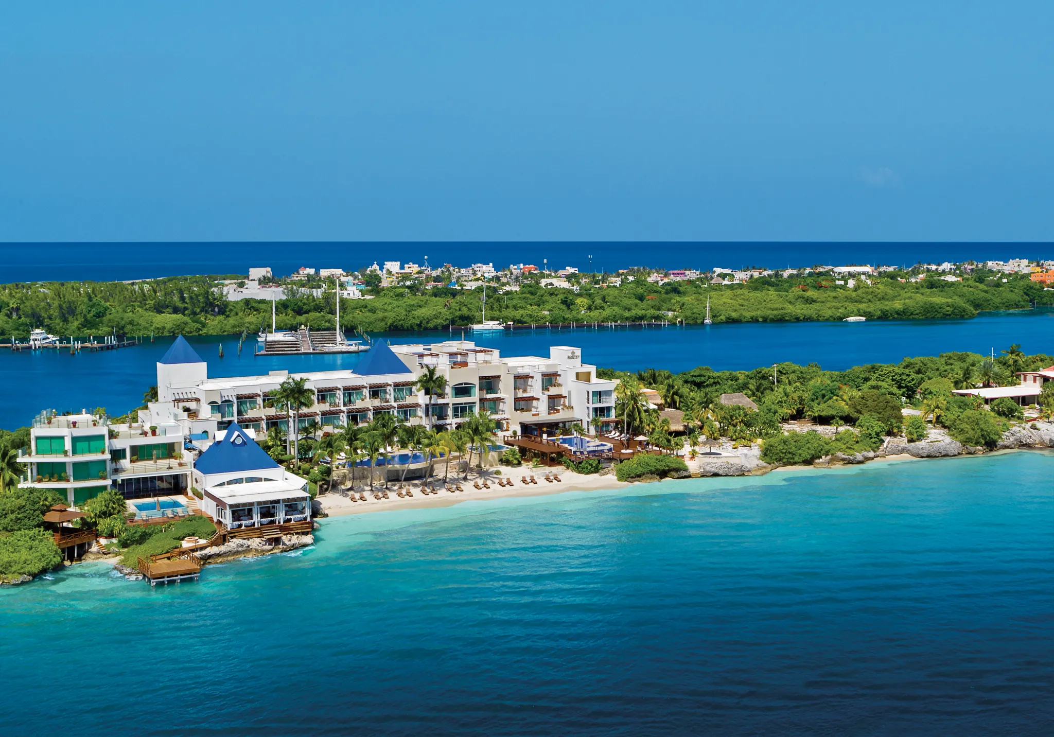 Coastal aerial view of Zoëtry Villa Rolandi with marina, beach, and vibrant Caribbean waters in Isla Mujeres.