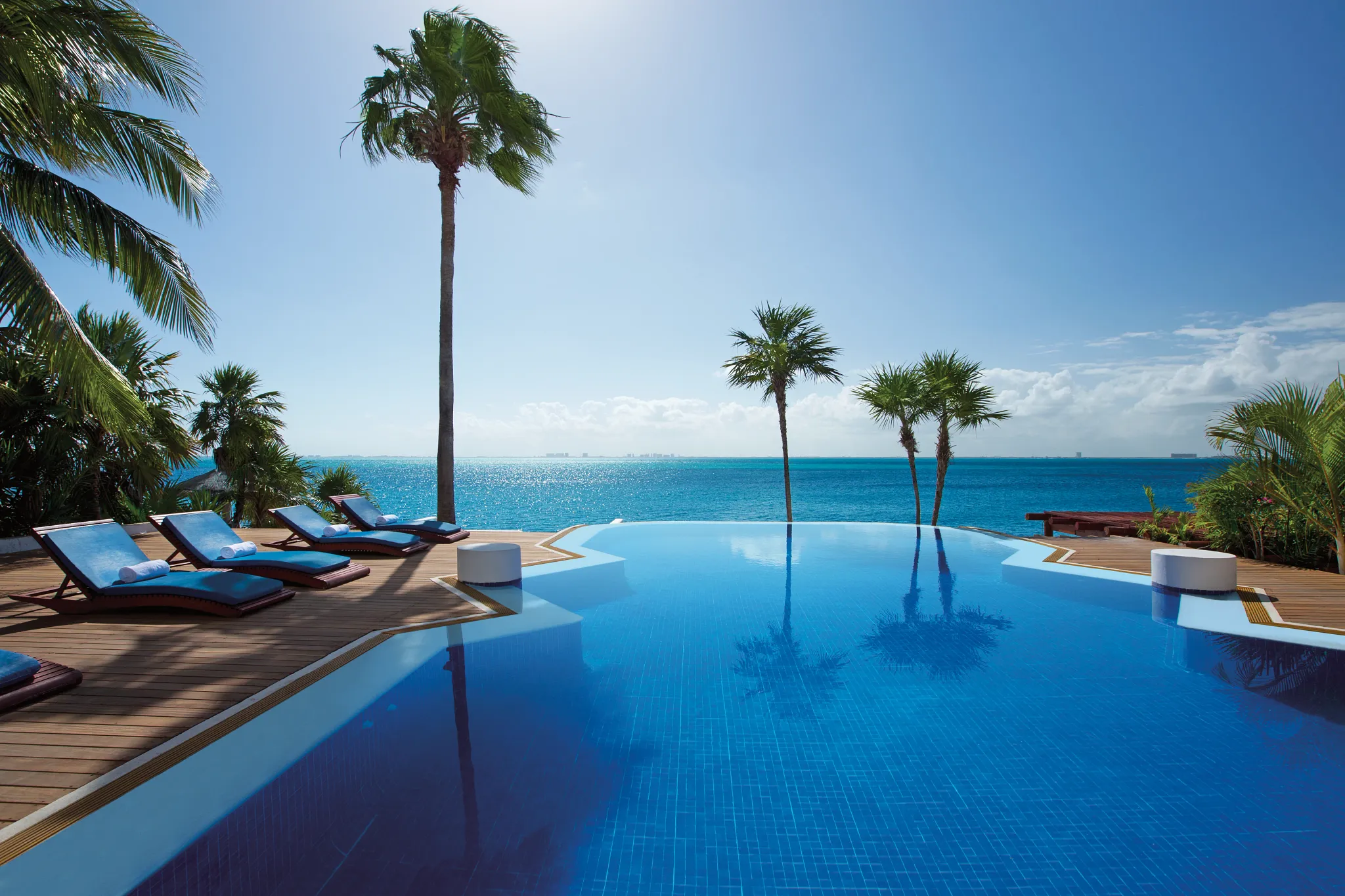 Oceanfront infinity pool surrounded by palm trees and lounge chairs at Zoëtry Villa Rolandi Isla Mujeres.