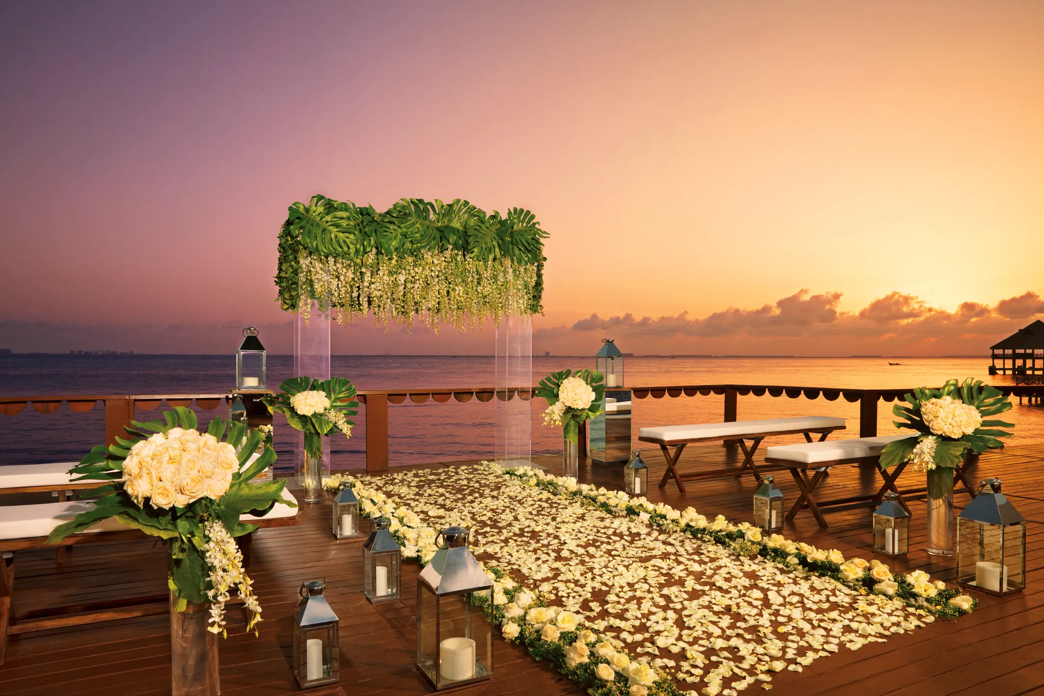 Sunset wedding ceremony setup with floral arch on oceanfront deck at Zoëtry Villa Rolandi Isla Mujeres
