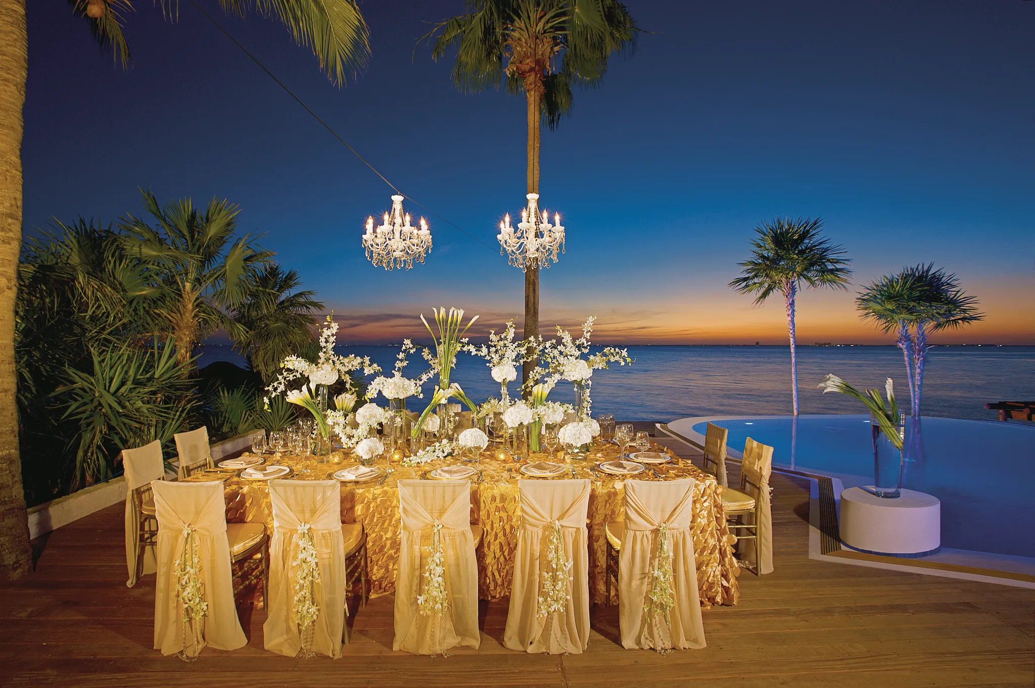 Elegant wedding reception table with gold linens and chandeliers overlooking the ocean at Zoëtry Villa Rolandi Isla Mujeres
